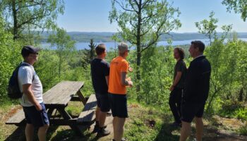 En grupp vandrare med ryggsäckar står på ett berg och tittar på utsikt över en sjö.