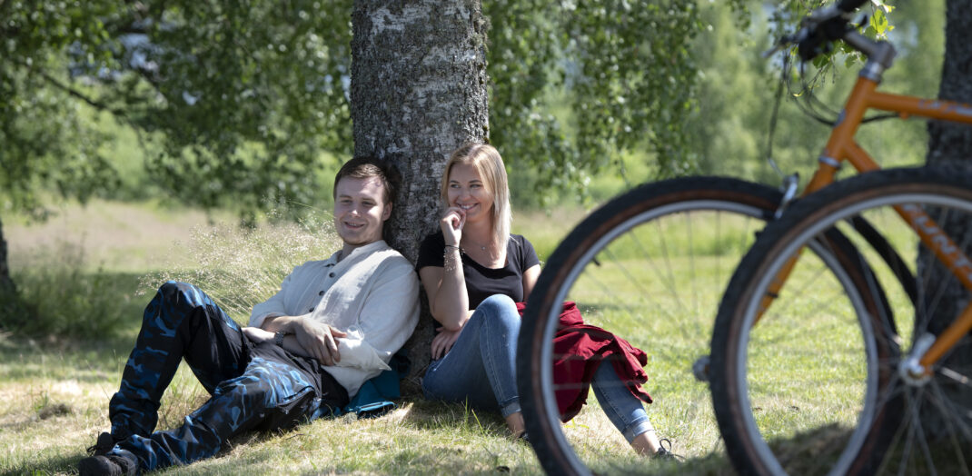 Ett par sitter och vilar vid björk allé under cykelresa i Sunne