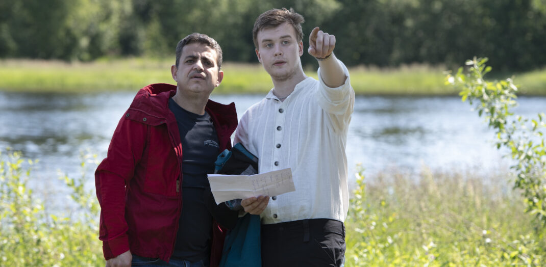 Två män står med sjön Fryken i bakgrunden. En pekar på något. En försöker se något.