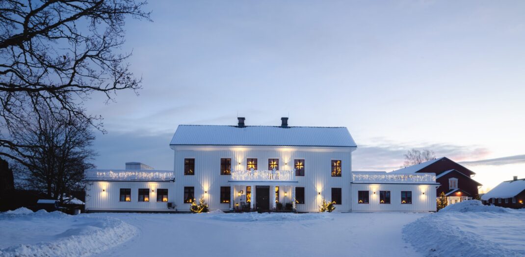 Ulvsby herrgård tidig vintermorgon i soluppgång. Snö på taket och marken. Julbelysning i fönster och ute.