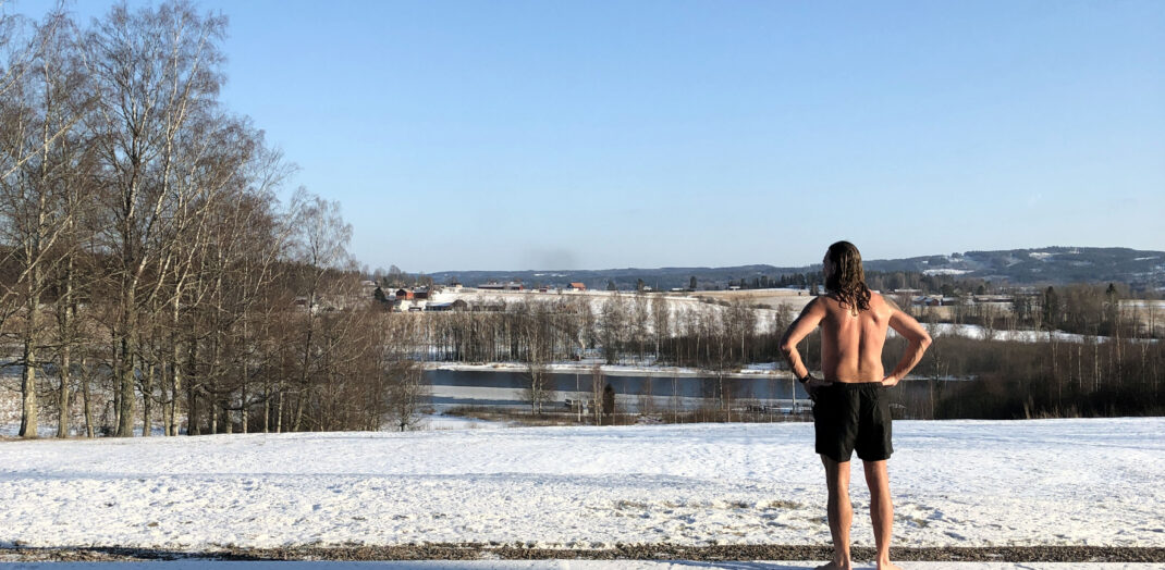 Man i bara badbyxor står ute i snön och ser ut över sjön Fryken. Svalkar sig efter bastubad i badstugan på Ulvsby herrgård. 