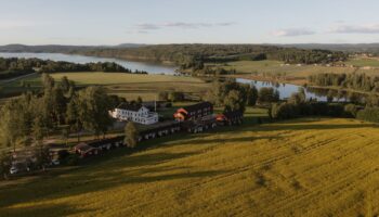 Flygbild på en vit herrgård, gula rapsfält och en blå sjö.